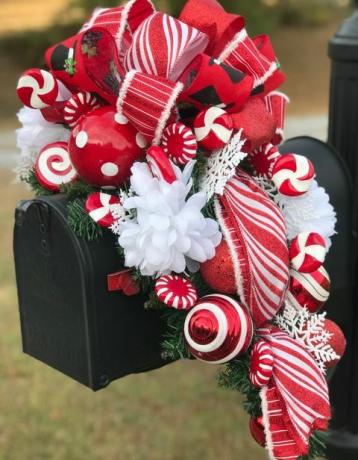 černá poštovní schránka s červenými a bílými tečkovanými a pruhovanými vánočními koulemi, stuhou a ozdobnými bonbony s bílými květy