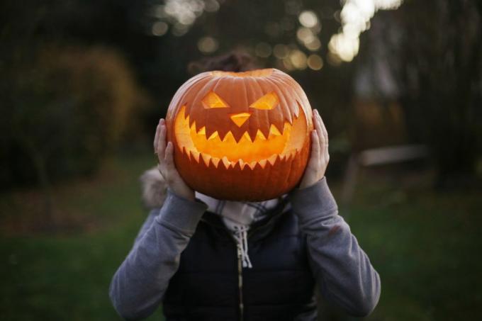 dívka držící vyřezávanou a osvětlenou halloweenskou dýni před hlavou