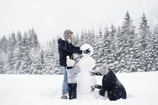 tříčlenná rodina staví sněhuláka ve sněhu