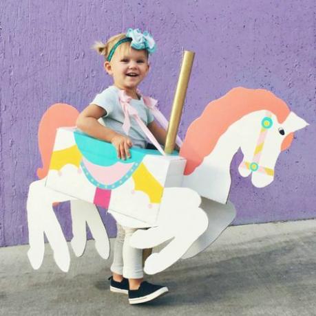 malá holčička s krabičkou tvarovanou a malovanou tak, aby vypadala jako kolotočový kůň kolem ní