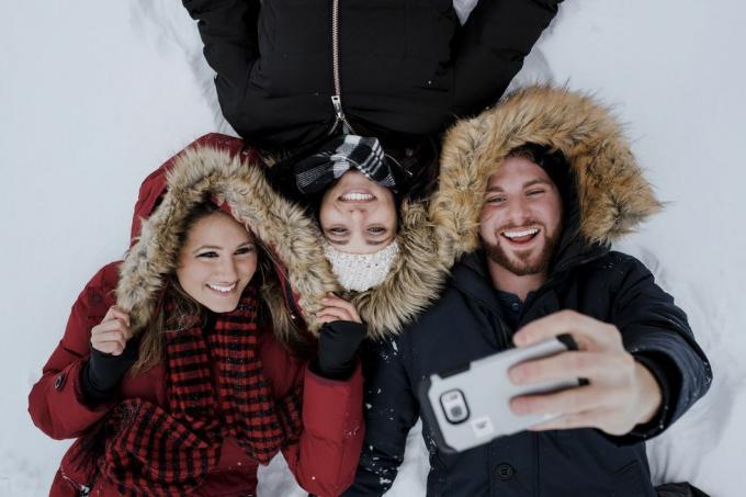 Vysoký úhel přátel, kteří si pořizují selfie, zatímco leží na zasněženém poli