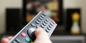 lidská ruka držící dálkové ovládání měnící kanály s televizí