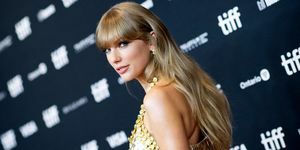 Taylor Swift se dívá přes rameno na červeném koberci ve zlatých šatech