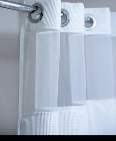 bílý sprchový závěs visící z chromové tyče na sprchový závěs