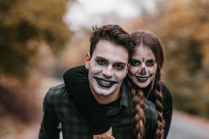 usmívající se muž v halloween make-up nesoucí usmívající se žena v halloween make-up na zádech