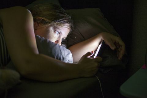 Žena při pohledu na chytrý telefon v posteli