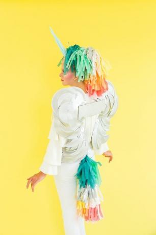 žena oblečená jako součást pegasu, část jednorožec s různobarevným papírovým ocasem a hřívou, bílými křídly a bílým rohem