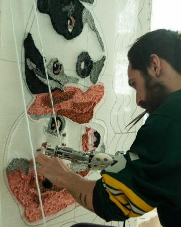 30letý španělský vousatý muž v rugbyovém dresu, ve své dílně pracuje na ručně vyráběných kobercích vyrobených z všívacích pistolí a akrylových vláken, s designem psího koberce