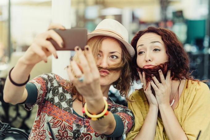 dvě přítelkyně drží vlasy přes obličej, aby vypadaly, jako by měly vousy a knír, a fotí si z toho selfie