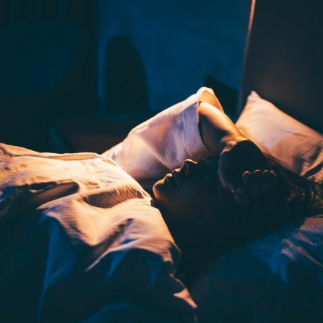 žena s nespavostí mladá žena leží na posteli s rukou na čele