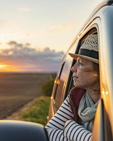 žena ve věku 40 let se kochá pohledem na krajinu ze svého karavanu, vypadá spokojeně a uvolněně