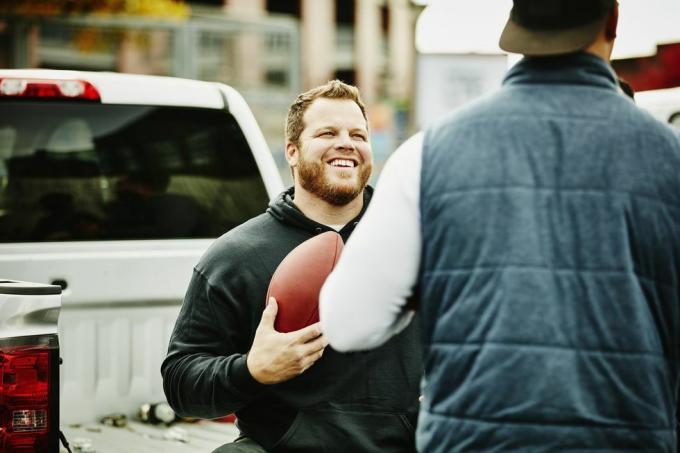 usmívající se muž, který držel fotbal s přítelem během tailgating party