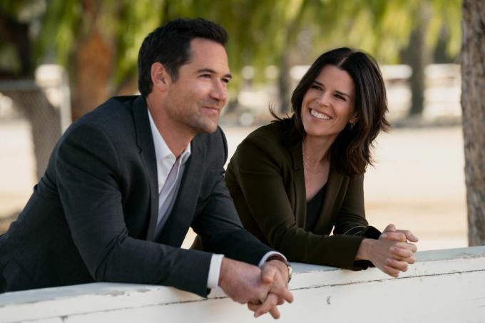 dvě postavy, které jsou bývalými manžely v seriálu, naklánějí se venku přes zeď, usmívají se a mluví
