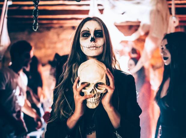 mladá žena s kostrou make-up drží lebku na halloween party